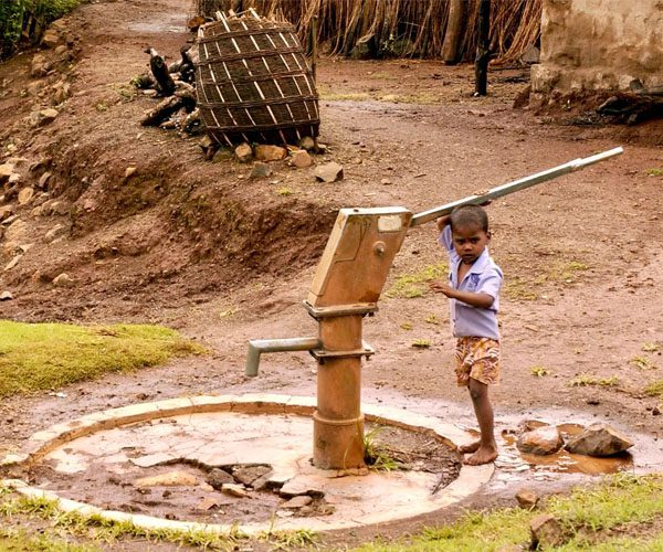 A young boy is standing at the water pump.